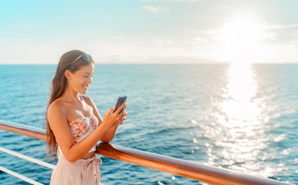 woman stands on boat in ocean using cellphone